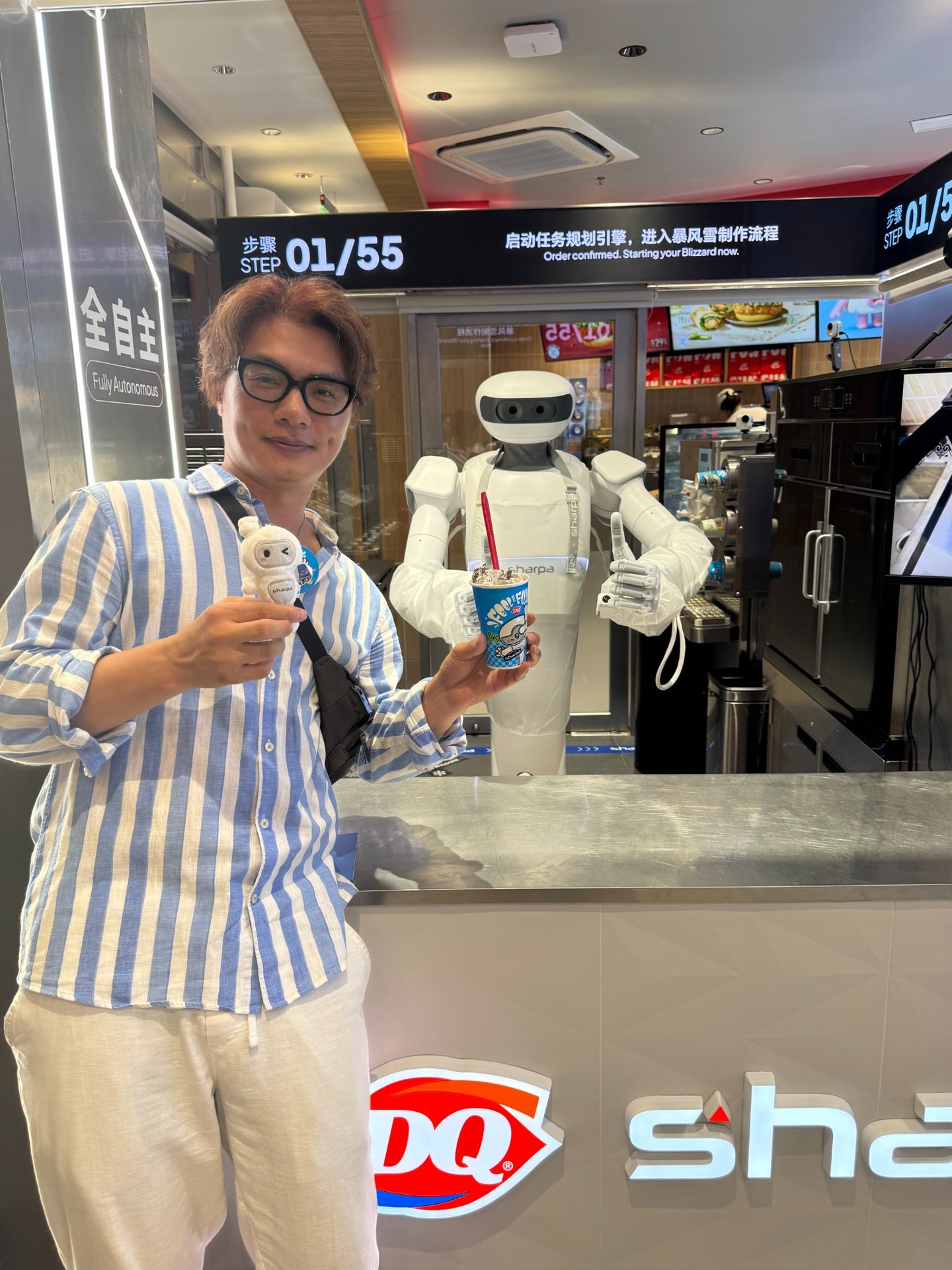 Henry Chan Jung在上海吴江路DQ门店手持暴风雪冰淇淋与Sharpa人形机器人合影